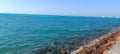 blue water and rocks, with boats in distance, viewed from the side walk Royalty Free Stock Photo