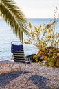 Blue white chair with hanging towel standing on the pebble beach of Garda lake under the palm tree with scenic view on endless Royalty Free Stock Photo