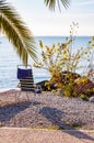 Blue white chair with hanging towel standing on the pebble beach of Garda lake under the palm tree with scenic view on endless Royalty Free Stock Photo