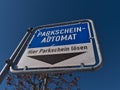 Blue and white colored sign with black arrow leading to the ticket machine of a public parking in town center.