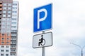 Blue and white parking sign with wheelchair for people with disabilities against sky and city buildings background. Royalty Free Stock Photo