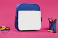 Blue and white school bag, colorful felt-tip pens in a stand, blue pins, magnifying glass and pencil cases on pink