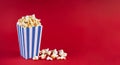 Blue white striped carton bucket with tasty cheese popcorn, isolated on red background