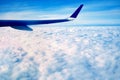 The blue wing of a large airplane, flying over the white morning clouds, at high altitude above the ground, against the blue sky Royalty Free Stock Photo