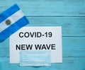 On a blue wooden background is a sheet with the inscription: covid -19 new wave, a medical mask and the flag of Argentina Royalty Free Stock Photo