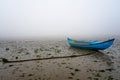 Blue wooden boat under a mud river in low tide with the rope that binds you to the ground with cloudy bottom of a day of fog. Royalty Free Stock Photo