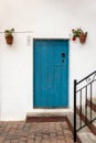 Blue wooden door on a white facade, typical house in a Spanish traditional village. Closed door with a metal handle, flower pots Royalty Free Stock Photo