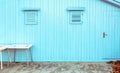 Blue wooden shed with small windows and two tables in front