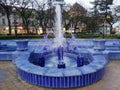 Blue working fontain in Subotica, Serbia in front of small park and city life.