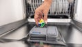 Blue, yellow and green dishwashing tablet put into the appliance by a female hand