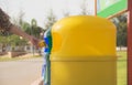 Blue and yellow plastic trashcan in the park at summer.