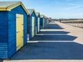 Blue and yellow wooden beach huts casting long shadows Royalty Free Stock Photo