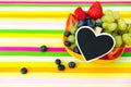 Blueberries, grapes and strawberries in a bowl on a striped table, black heart