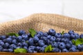 Blueberries With a Green Mint leaf in a Wooden Bowl on a white with piece of cloth top view, Summer Freshly Berry