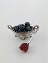 Blueberries in an old silver bowl decorated with swans. Raspberry on a silver antique spoon. White background.