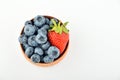 Blueberries and one strawberry in wooden bowl isolated on white Royalty Free Stock Photo