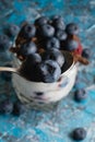 Blueberries in a teaspoon close-up and fancy delicious dessert with chocolate, yogurt and raspberry in a glass cup on a