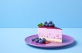 Blueberry cheesecake with fresh berries on top on a plate over minimalist blue background with copy space