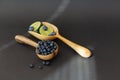 Blueberry fruits with limes on a wooden spoon against a dark background.