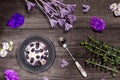 Blueberry Graham Cheesecake topped with fresh berries alongside a spoon on a dark wood background with purple flowers and twigs.