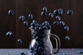 Blueberry levitation. Flying berries near a glass jug on a dark wooden background. Healthy, light blueberry creative concept