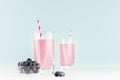 Blueberry milkshakes in transparent glass with blueberries in bowl, striped straw on white wood table and mint color wall.