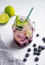 Blueberry Mojito Or Lemonade With Lime, Ice And Mint In A Glass On A Light Background With Berries And Fruit Close Up. The Concept