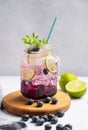 Blueberry Mojito Or Lemonade With Lime, Ice And Mint In A Glass On A Wooden Board On A Light Background With Berries And Fruit.