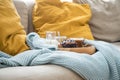 Blueberry muffin with coffee, sugar and milk on wooden tray and comfy sofa with blue wool knit blanket and yellow cushions Royalty Free Stock Photo