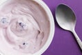 Blueberry yogurt in plastic cup on purple background with metal spoon - top view close up photo of yoghurt in plastic pot Royalty Free Stock Photo