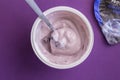 Blueberry yogurt with spoon in plastic cup with foil lid on side isolated on deep purple background - top view Royalty Free Stock Photo