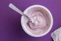 Blueberry yogurt with spoon in plastic cup with foil lid on side isolated on deep purple background - top view Royalty Free Stock Photo