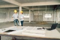 Blueprint, laptop computer, and industrial tools at construction site with two engineers or architects working in background