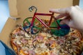 blur effect, woman hand cutting delicious pizza in carton box on table, bicycle pizza cutter knife on cheese in cardboard