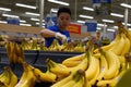 Blur motion of clerk stocking banana on display rack inside superstore produce department