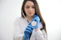 Blur portrait of young alluring nurse with long hair in white medical uniform with focus on stethoscope on neck standing