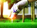 Blur the white ball on the tee Closely there is the golfer`s hand on the green lawn Royalty Free Stock Photo