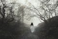 A blurred, abstract ghostly woman. walking through a forest on a spooky, misty winters day. With an out of focus, moody edit