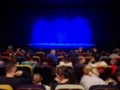 Blurred abstract image. Auditorium of the theater. Parents with children before the show. Blue curtain on stage