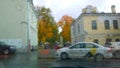 Blurred abstract image of autumn city street, apartment building, orange trees and cars through glass window with raindrops. Rainy