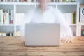 Blurred adult man working in front of laptop from home at wooden table and bookshelf full of books Royalty Free Stock Photo