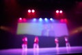 Blurred background of a dance scene with silhouettes of children dancing and a screen in the background. Bright stage