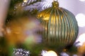 Green beautiful ball on a pine Christmas tree branch. Blurred background and garland with yellow light. Soft focus