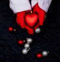 Blurred background. Hands in red mittens hold the heart. Santa Claus hands hold a red Christmas tree toy on a black background. Ch Royalty Free Stock Photo