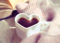 Blurred background of morning still life, coffee in bed. White cup in shape heart and fluffy scarf. Shadow and sunlight. At home. Royalty Free Stock Photo