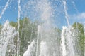 Blurred background with splashing fountain water against a blue sky and green trees. Pure refreshing water in summer heat Royalty Free Stock Photo