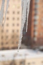 Blurred background of a winter cityscape with apartment buildings in snow. Few of icicles in the foreground in defocus.