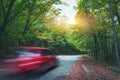 Blurred car going mountain road in summer forest at sunset