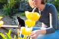 Blurred caucasian blonde smiling woman sitting and cutting yellow tulips in the garden. In the background, a garden and black cat Royalty Free Stock Photo