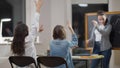 Blurred Caucasian teacher writing on chalkboard as schoolgirls raising hands to answer. Smart nerds sitting at desk in